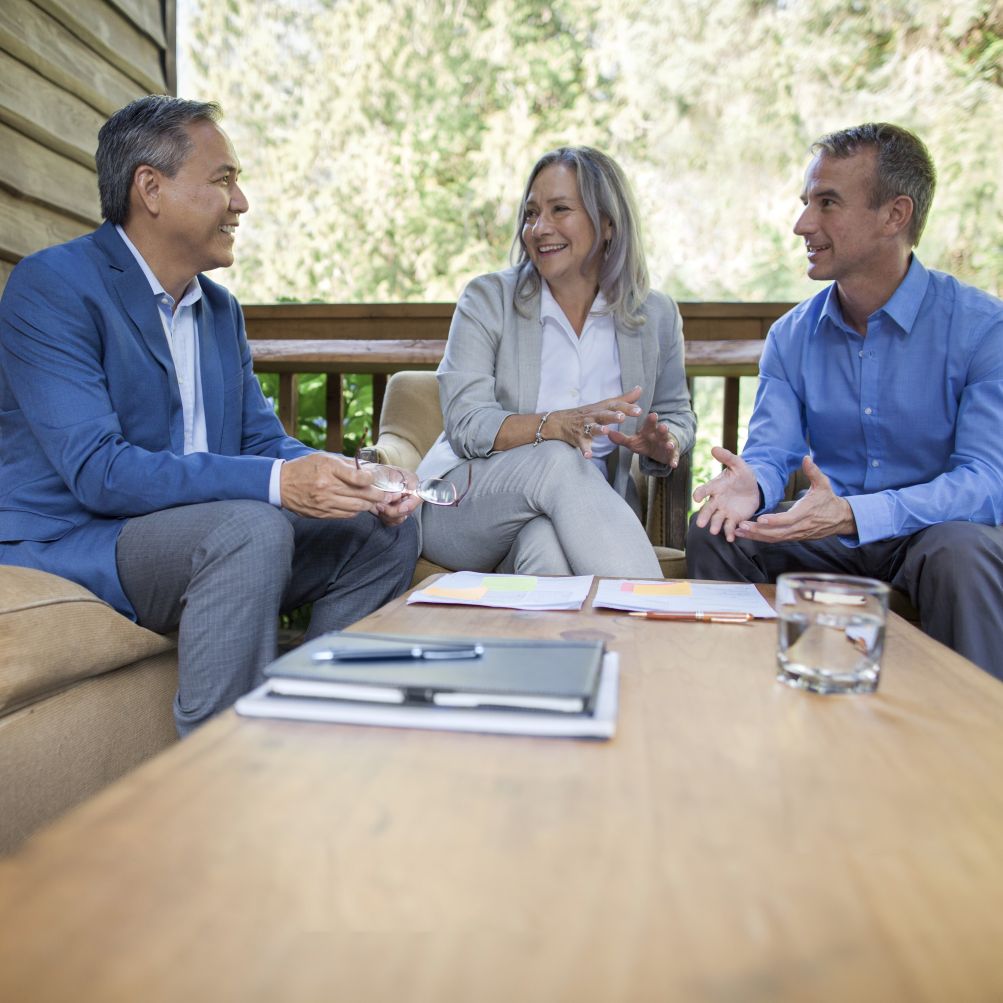 two men and woman talking around a table with outdoor background