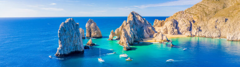 ocean with sailboats by cliffs and rock formations