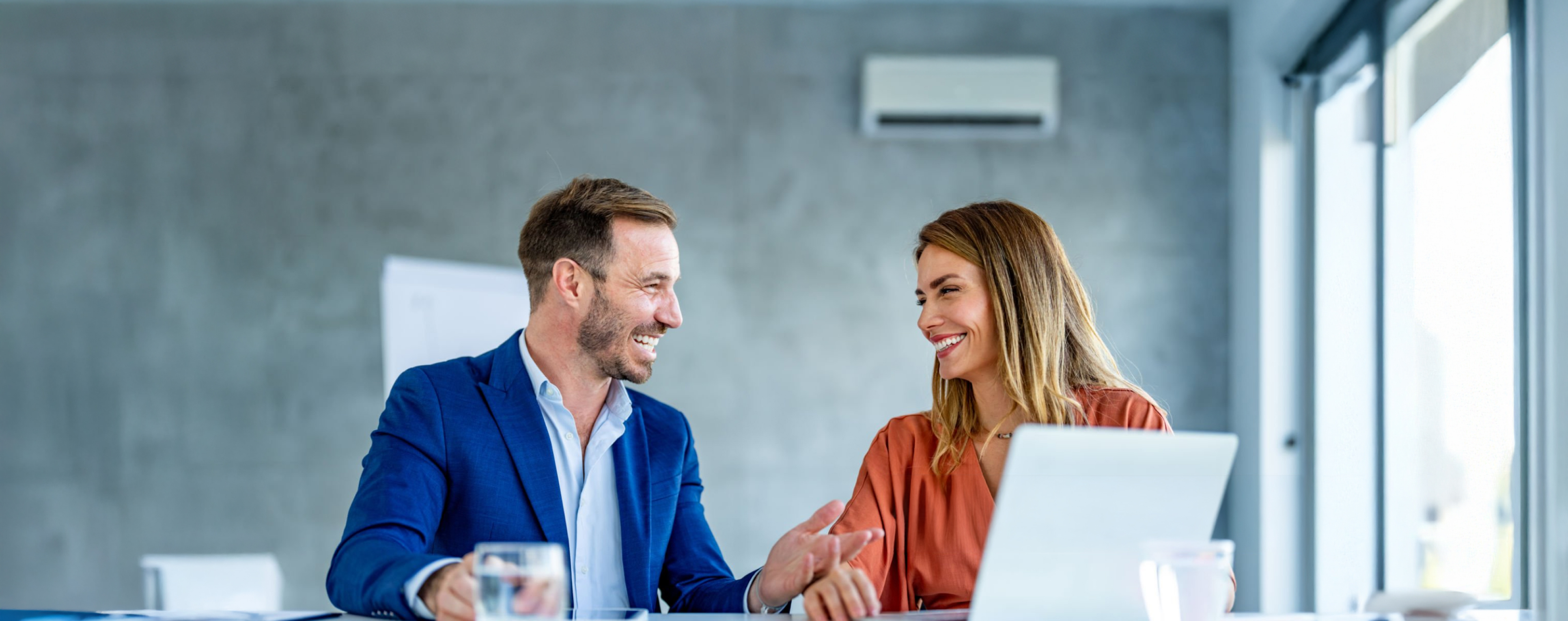 man and woman sitting at a desk smiling in front of a laptop